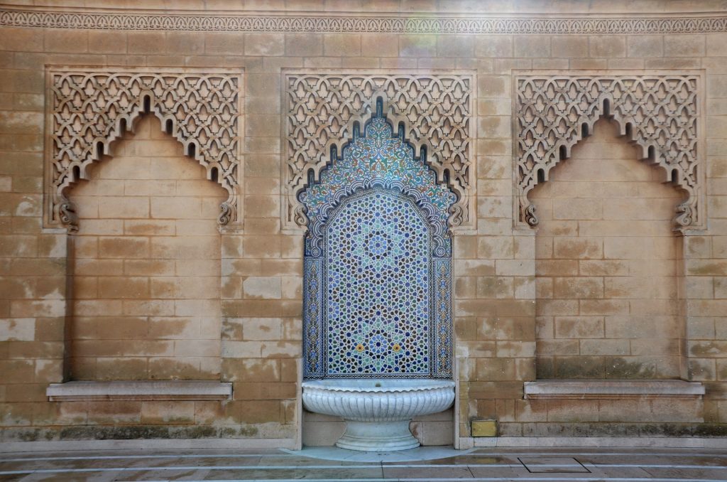 Fontaine traditionnelle avec mur en pierre avec des arabesques.